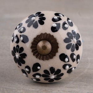 May include: A white ceramic knob with a black floral pattern and a brass accent. The knob is round and has a smooth surface.