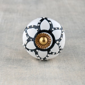 Może przedstawiać: Biały ceramiczny gałka z geometrycznym wzorem w kolorze czarnym i białym. Gałka ma złoty środek.