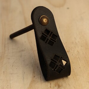 Puede incluir: Tirador de cajón de cuero negro con un tornillo de latón y un diseño de corte geométrico.