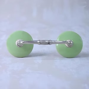 Puede incluir: Un par de tiradores de cajón de cerámica verde con una barra de metal plateado que los conecta.