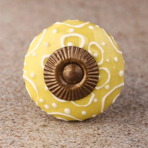 May include: A yellow ceramic knob with a white floral design and a gold metal base.