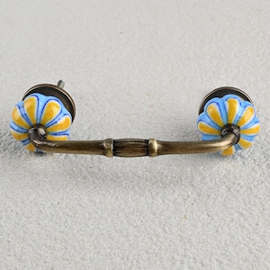 May include: A brass drawer pull with blue and yellow ceramic knobs. The knobs have a floral design.