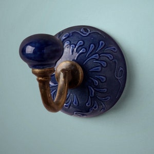 Könnte beinhalten: Ein blauer Keramikhaken mit floralem Design und einem Messinghaken. Der Haken ist an einer Wand montiert.
