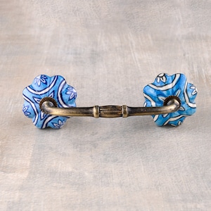 May include: A blue and white ceramic drawer pull with a floral pattern. The pull has a brass bar connecting the two ceramic pieces.