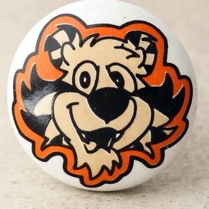 May include: White ceramic knob with a cartoon tiger face in orange, black, and tan. The tiger has a friendly expression with a wide smile and large eyes.