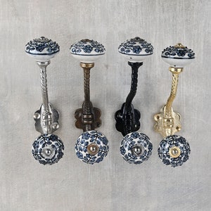 May include: Four wall-mounted coat hooks featuring white ceramic knobs with blue floral patterns. Each hook has a twisted metal stem and a decorative base plate. The metal finishes include polished silver, antique bronze, matte black, and gold.