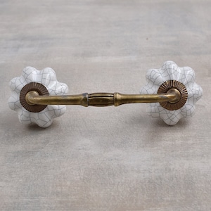 May include: White ceramic drawer pull with a crackled glaze finish and a brass bar connecting the two knobs.