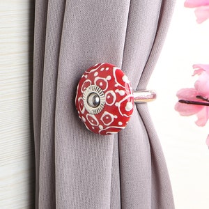 May include: Red and white ceramic curtain tieback with a silver metal ring. The tieback has a floral pattern.