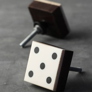 以下が含まれることがあります： 2つのキャビネットノブ、1つは黒と白のサイコロで、5つの黒い点があります。もう1つは黒い正方形のノブです。