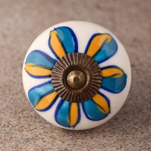 May include: White ceramic knob with a blue and yellow flower design and a brass screw.