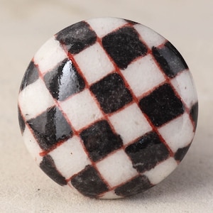 Peut inclure: Un bouton rond en céramique avec un motif en damier noir et blanc et des lignes rouges. Le bouton a une finition brillante.