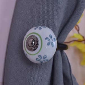 May include: White ceramic curtain tieback with a green and silver ring and a blue floral pattern.