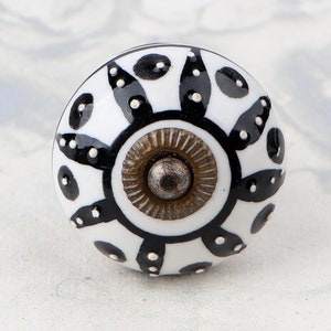 May include: White ceramic knob with a black and white geometric design. The knob has a brass base with a metal screw.