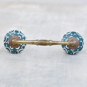 May include: A green ceramic drawer pull with a white floral pattern. The pull has a brass bar connecting the two knobs.