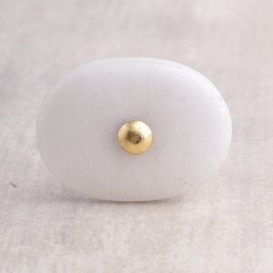 Op de afbeelding: Witte ovale keramische kastknop met een gouden metalen centrum.
