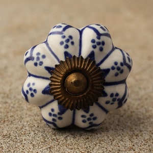 May include: A white ceramic knob with a blue and white floral pattern and a gold metal base. The knob is shaped like a flower.