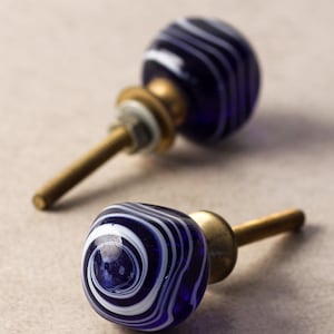 May include: Two blue and white glass cabinet knobs with brass screws. The knobs have a swirling pattern.