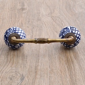 May include: A blue and white ceramic drawer pull with a brass bar connecting the two knobs. The knobs have a geometric pattern and are accented with gold.