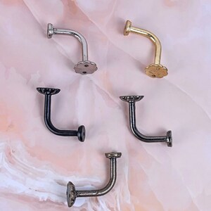 May include: Five decorative wall hooks in different finishes: silver, gold, black, and bronze. Each hook has a curved arm and a decorative flower-shaped base.