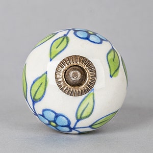 May include: White ceramic knob with a blue and green floral design. The knob has a brass screw hole in the center.