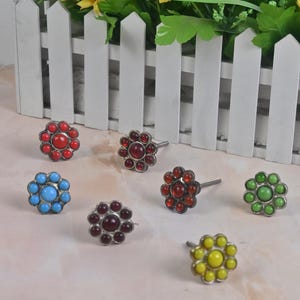 May include: Assortment of colorful flower-shaped cabinet knobs with a silver finish. The knobs have a single screw for installation.