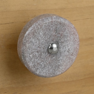 Könnte beinhalten: Ein runder, grauer Stein-Knopf mit einem silbernen Metallkern. Der Knopf ist auf einer hellbraunen Holzoberfläche montiert.