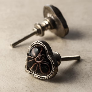 Puede incluir: Dos tiradores de armario en forma de corazón con fondo oscuro y diseño de telaraña en bronce. Los tiradores tienen un acabado metálico plateado y un tornillo para la instalación. Herrajes decorativos para muebles.