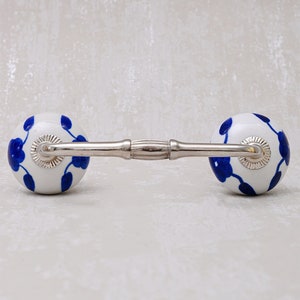 Op de afbeelding: Een witte keramische ladegreep met een blauw bloemenontwerp en een zilveren metalen verbindingsstang.