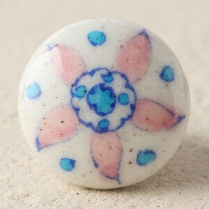 Puede incluir: Pomo de cerámica blanco con un diseño floral rosa y azul. El pomo tiene un acabado blanco moteado y un centro azul y blanco.