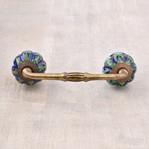 Puede incluir: Un tirador de armario de latón con dos pomos de cerámica azul y verde. Los pomos tienen un patrón floral.