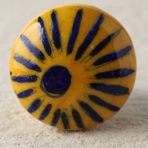 May include: A yellow ceramic knob with a blue and black sunburst design.