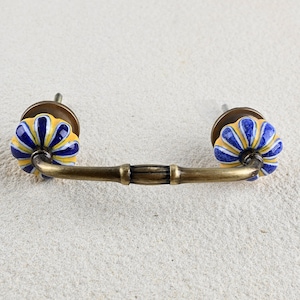 May include: A brass cabinet pull with two yellow and blue ceramic knobs. The knobs have a floral design.