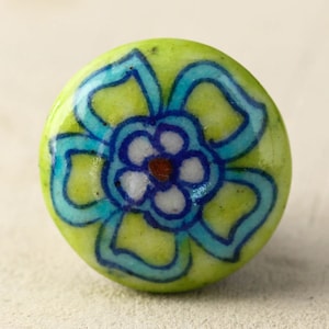 May include: A green ceramic knob with a blue and white floral design. The flower has a white center with a brown dot in the middle.