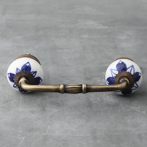 May include: A pair of white ceramic drawer pulls with blue floral designs and a brass arch connecting them.