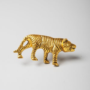 以下が含まれることがあります： 歩いているポーズの虎の金色の金属製フィギュア。フィギュアは縞模様で、表面にテクスチャが施されています。