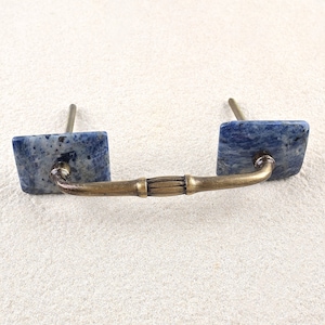 Puede incluir: Un par de tiradores de armario cuadrados azules y blancos con una barra de latón que los conecta.