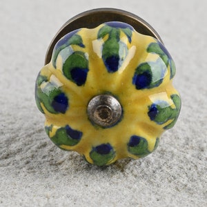 Könnte beinhalten: Gelber Keramik-Knopf mit grünem und blauem Blumenmuster. Der Knopf hat eine Messingbasis.