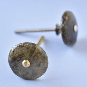 May include: Two round, gray, stone cabinet knobs with gold accents. The knobs are attached to silver screws.