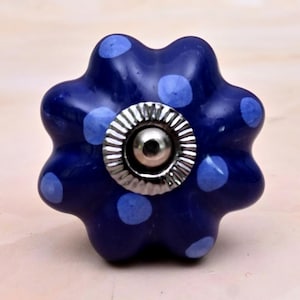 Puede incluir: Un pomo de cajón de cerámica azul oscuro con forma festoneada de flor y lunares azul claro. El centro presenta una pieza de metal plateado circular con un borde estriado y una cúpula lisa y reflectante en el medio.