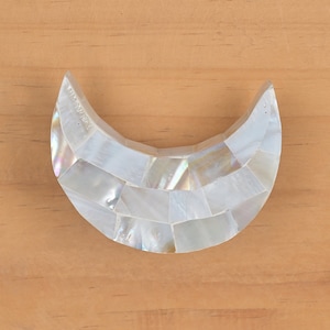 Op de afbeelding: Een witte halve maanvormige kastknop gemaakt van iriserende parelmoer tegels.