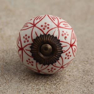 May include: White ceramic knob with a red floral pattern and a brown metal base.