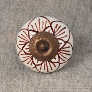 Puede incluir: Pomo de cerámica blanco con un diseño floral marrón y un centro de latón.