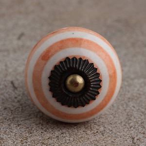Può includere: Un pomello in ceramica a strisce bianche e arancioni con un accento in metallo nero e un centro dorato.