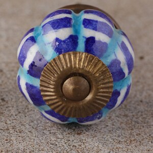 May include: A decorative cabinet knob with a blue and white striped pattern. The knob has a round, floral shape with a brass base. The blue stripes are in varying shades, and the knob is likely made of ceramic.