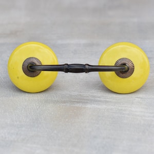 May include: A yellow ceramic drawer pull with a black metal bar connecting the two knobs.
