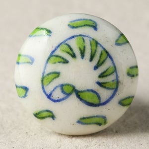 Könnte beinhalten: Weißer Keramik-Knopf mit einem blauen und grünen floralen Design. Der Knopf ist rund und hat ein sich wiederholendes Muster aus Blättern und Spiralen.