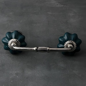 May include: A dark green ceramic drawer pull with a silver metal bar connecting the two knobs. The knobs have a fluted design.