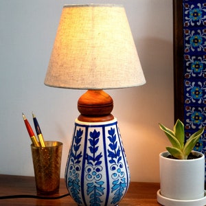 May include: A blue and white ceramic table lamp with a floral design. The lamp has a wooden base and a white linen lampshade.