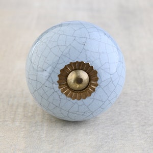 Puede incluir: Un pomo de cerámica azul claro con un esmalte craquelado y una base de metal dorado.