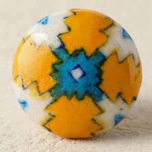 May include: A round ceramic knob with a white, yellow, blue, and green geometric pattern.